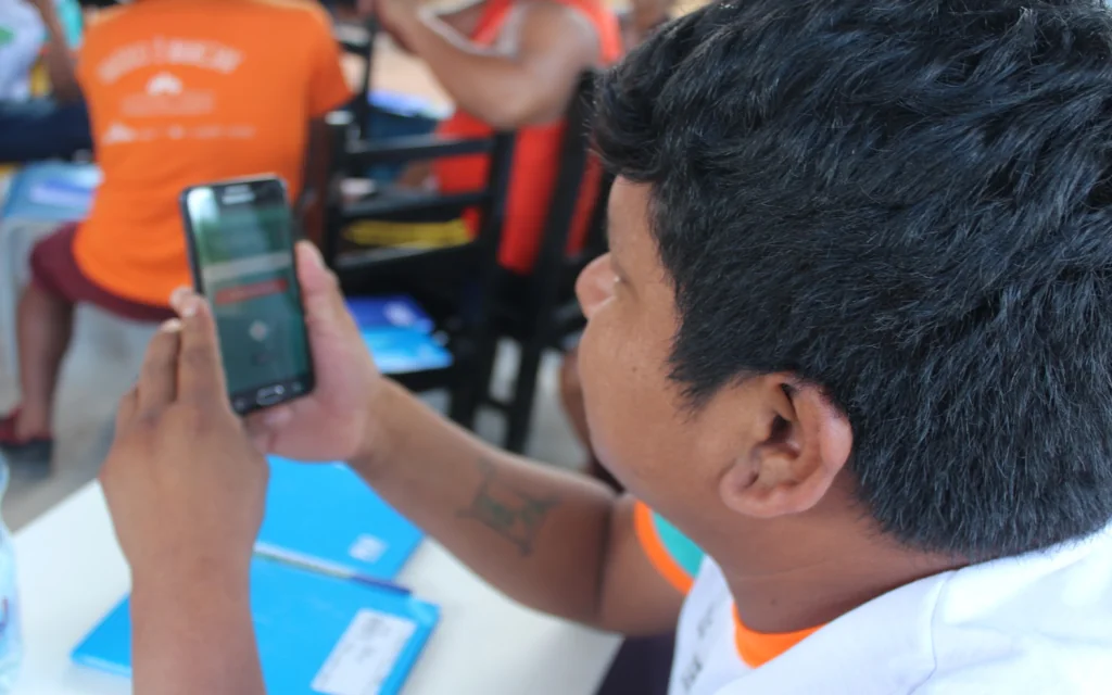 Pessoa indígena segura celular em que acessa SOMAI. Celebração de 10 anos do SOMAI ocorrerá em outubro.